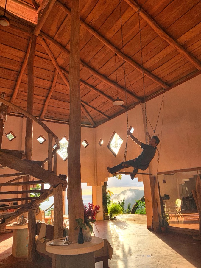 Steven hanging from a rope inside a tall open-air wooden house in Costa Rica
