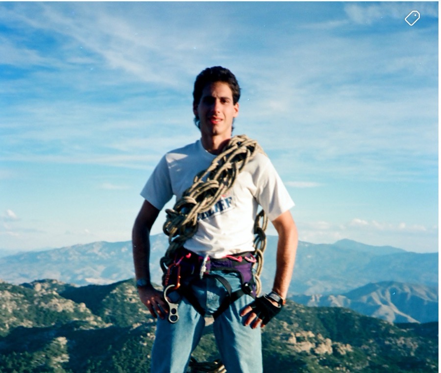 Young Steven on a summit in a climbing harness, a coiled rope over his shoulder