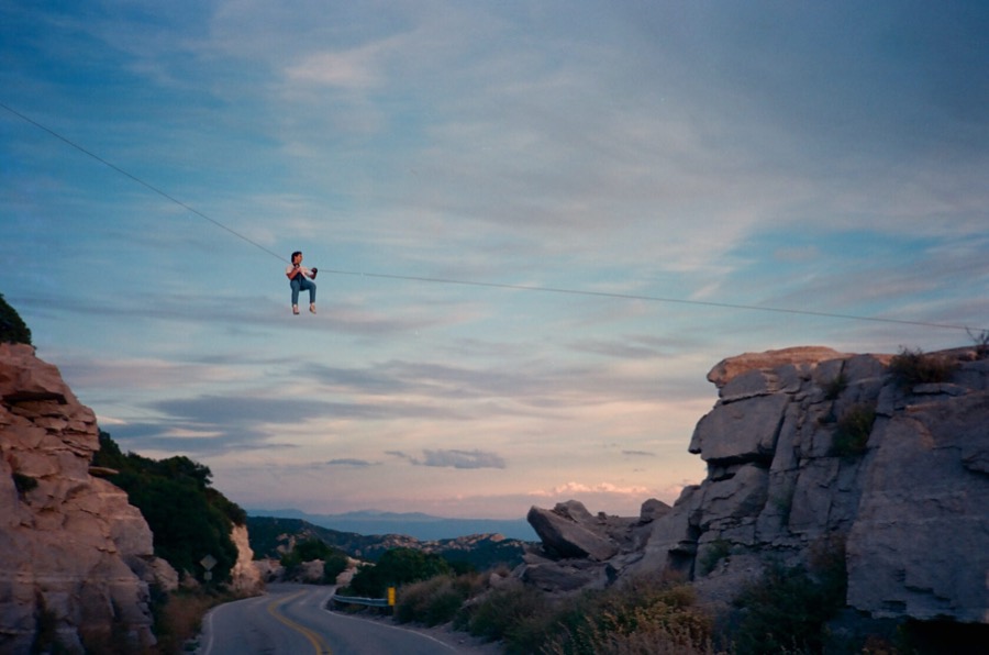 A tiny figure hanging on a line high above a road between rock outcrops