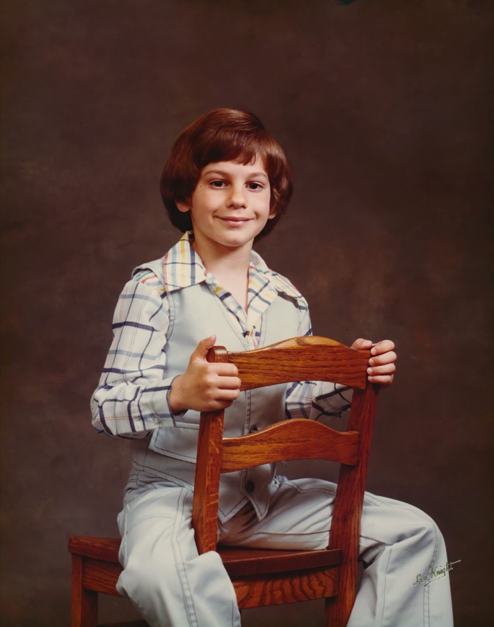 Steven as a young boy in a studio portrait, sitting on a wooden chair