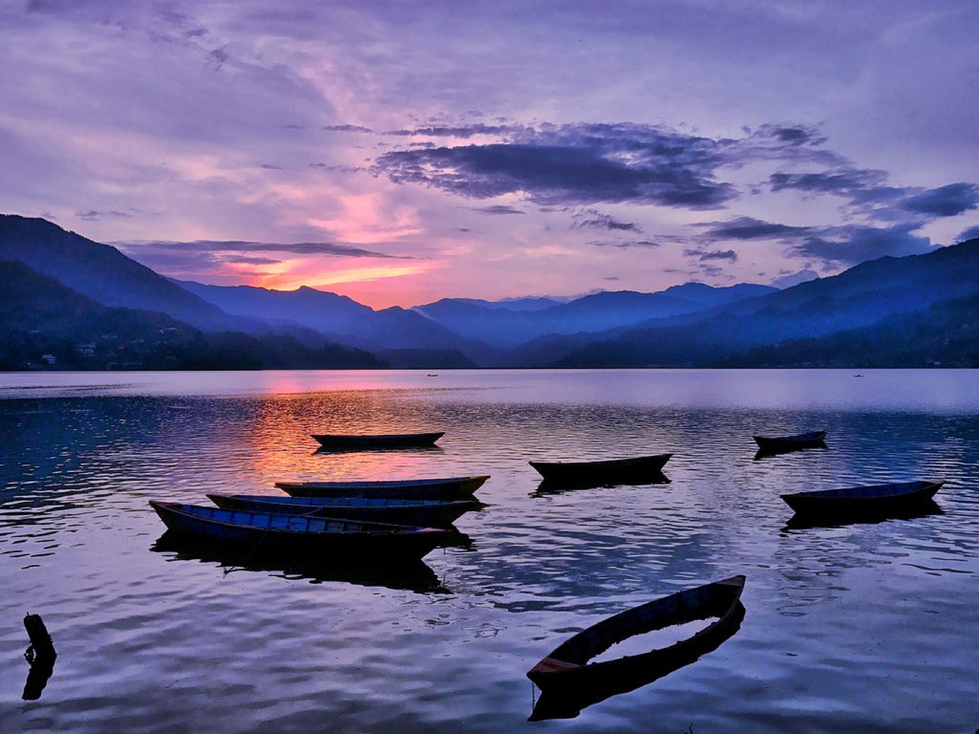 Small wooden boats on Fewa Lake at dusk under a pink sky